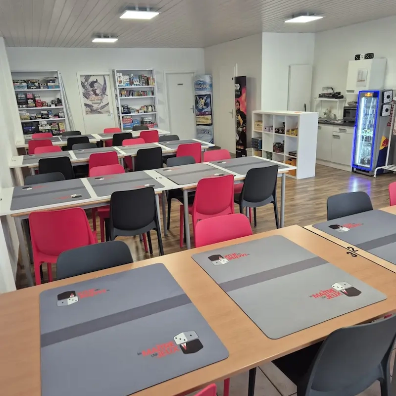 Espace avec des tables, un frigo à boisson et des étagères de jeux